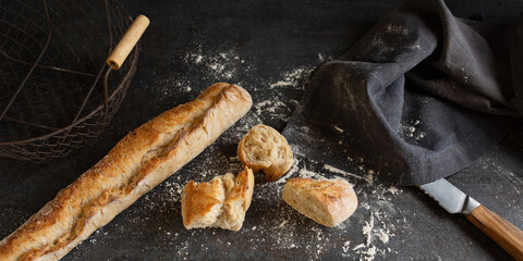 Freshly baked french baguette in a basket on a black kitchen table with flour and bread knife....
