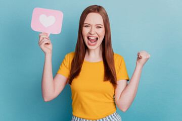 Portrait of astonished excited lady hold heart icon card raise fist scream on blue background