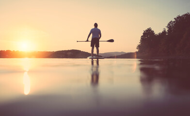 Rear view of man floating on the lake on paddle board