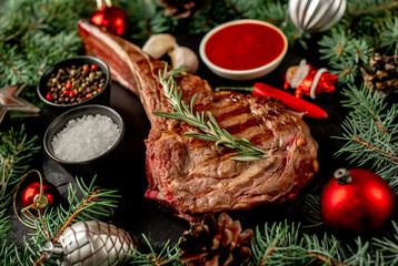 Grilled Christmas tomahawk steak with fir tree and tree decorations on stone background