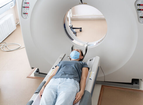A woman in a medical mask lies on the tomograph table. woman is undergoing computed axial tomography examination in a modern hospital.