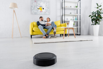 Robotic vacuum cleaner on floor near blurred couple in living room