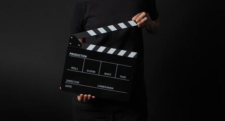 Woman hand is holding black clapperboard on black background. In studio shooting.