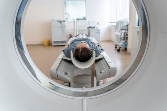 A woman in a medical mask lies on the tomograph table. woman is undergoing computed axial tomography examination in a modern hospital.