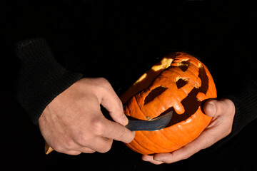 Halloween decor preparation and human concept. Close up hands carving pumpkin. Black background. Text Space.