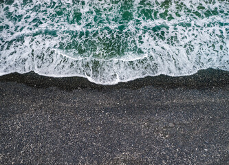 Stormy weather, sea waves breaking on a shore with volcanic black sand, background with copy space