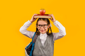 Back to school kid. Happy child holds a book and a red Apple in her head on a yellow background. Education and intellectual development of children. World book day.