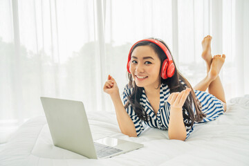 Beautiful young woman relaxing and listening the music while using laptop computer on the bed in bed room with copy space. Beauty asian girl gets happy, relaxing. She enjoying life.