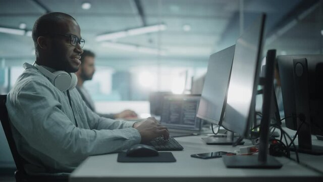 Diverse Office: Black IT Programmer Working on Desktop Computer. Male Specialist Creating Innovative Software Engineer Developing App, Program, Video Game. Terminal with Coding Language. Arc Shot