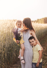 Mother with children with her son and daughter walking through a field of wheat