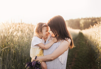 Mom holds her little daughter in her arms in a wheat field in the summer