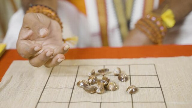 Close up shot of astrologer hands placing cowrie shells on chart and counting to predict future - Concept of Indian horoscope or fortune telling