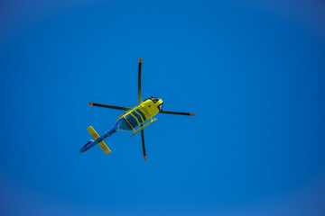 Naklejka na ściany i meble Yellow emergency helicopter over blue sky