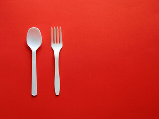 赤い紙の上に縦に置いたプラスチックスプーンとフォーク