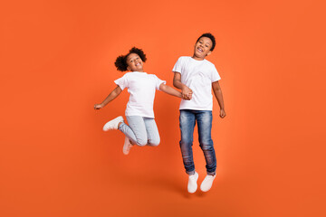 Full size photo of small funny girl boy jump wear white t-shirt jeans sneakers isolated on orange background