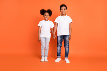 Full body photo of small sweet girl boy hold hands wear white t-shirt jeans sneakers isolated on orange background
