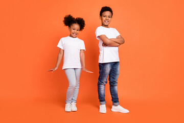 Full length photo of little cool girl boy crossed arms wear white t-shirt jeans sneakers isolated on orange background - Powered by Adobe