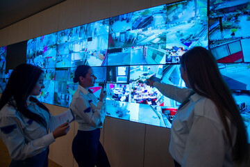 Security guards standing in front of a large CCTV monitor at the main control room while reading...