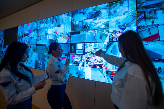Security guards standing in front of a large CCTV monitor at the main control room while reading and discussing plans