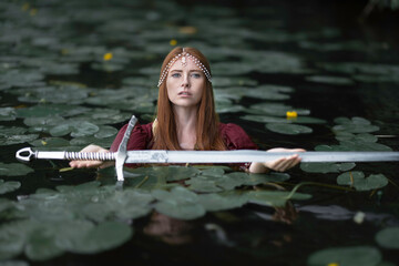 The mistress of the lake among the leaves of water lilies gives a medieval sword