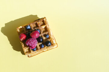 A waffle with different berries of black and red color on a yellow background is hard light. Homemade cakes crispy waffles on a colored background top view of kopi space