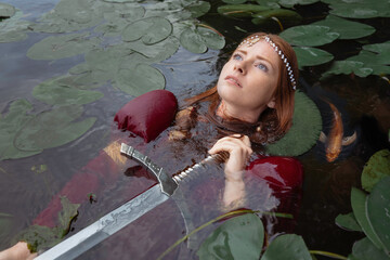 The mistress of the lake among the leaves of water lilies lies on the water with a sword on her...