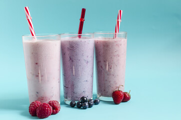 Milkshakes with the addition of raspberries, strawberries and blueberries on a light background close-up. Cocktails made of ice cream, milk and berries on a blue background