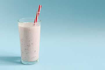A milkshake in a transparent glass with a red tube on a bright blue background close-up. Cocktail of ice cream, milk and berries on a colored background place for text