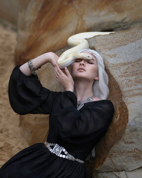 White-haired girl in a black dress with a white snake crawling on her face