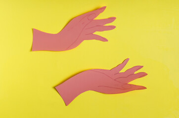 Obraz premium Two palms made of red paper on a bright yellow background of the mine space. The concept symbol consists of two hands holding an empty space on a colored background