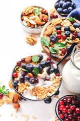 Muesli bowl and organic ingredients for healthy breakfast. Granola, nuts, blueberry, cranberry, oatmeal, greek yoghurt, whole grain flakes on white table