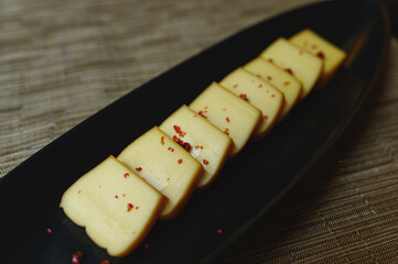 Smoked cheese sprinkled with chopped chilli Placed in a black plate on a wooden table.