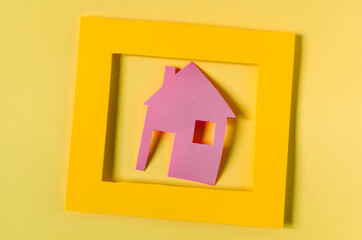 Cardboard house in an orange frame on a light background. The concept of a mortgage.