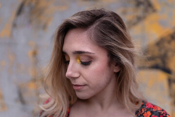 Blonde young girl model posing closing her eyes in front of a yellow graffiti wall