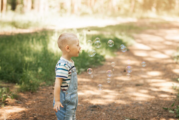 Naklejka premium Little boy inflating soap bubbles in the summer in nature