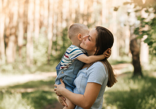 A young mother holds in her arms and hugs a little boy in the summer in nature