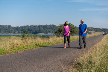 young woman and senior man wearing protective masks and walking outside on a sunny day
