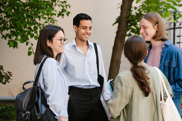 Multiracial young students talking to each other while standing outdoors