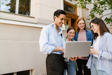Multiracial students using laptop and laughing while standing outdoors