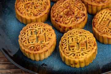There are moon cakes on the plate of the wood grain table. The moon cakes are engraved with  
