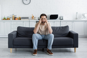 Man sitting with closed eyes on couch while suffering from headache