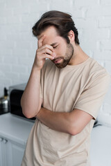 Sick man with closed eye standing in kitchen