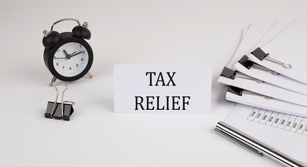 Card with text TAX RELIEF on a white background, near office supplies and alarm clock. Business concept.