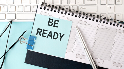 BE READY text on blue sticker on planning and keyboard,blue background