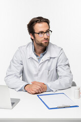 doctor sitting near clipboard, laptop and container with pills isolated on white, medical cannabis concept