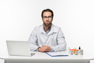 doctor in eyeglasses near laptop, clipboard and medical cannabis medication isolated on white