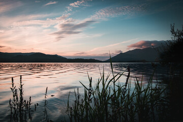 A view from the shoreline of Derwentwater in the lake District, looking over the water at sunset and the hills and mountains that encapsulate the area.