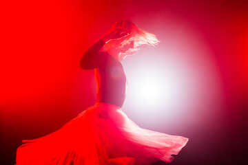 ballerina with a white dress and black top posing on red smoke background © Nikola Spasenoski
