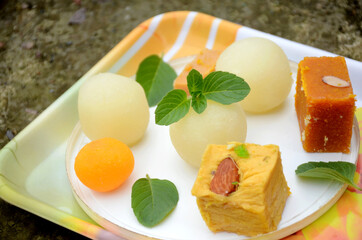 closeup the bunch yellow gram flour sweet,syrup filled ball, brown condensed milk sweet with green mint over out of focus white brown background.