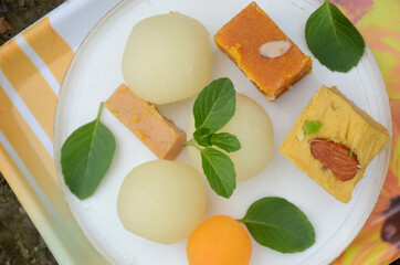 closeup the bunch yellow gram flour sweet,syrup filled ball, brown condensed milk sweet with green mint over out of focus white brown background.